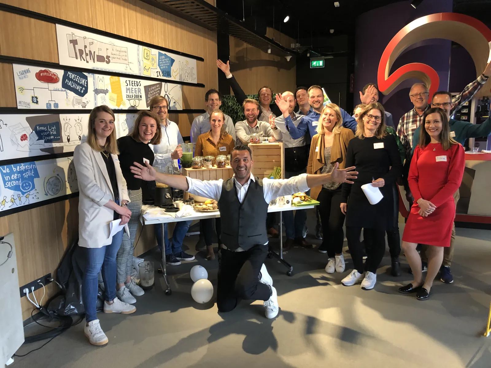 Jean-Marc geknield voor een enthousiast team bij een tafel vol groente, fruit en blenders tijdens een Smoothieclub-workshop