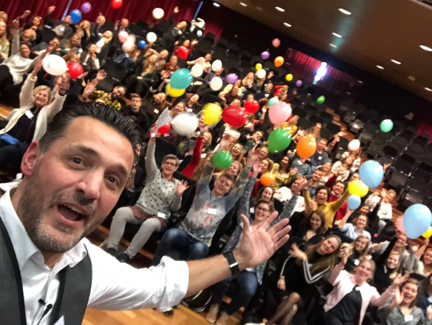 Jean-Marc maakt een selfie met een grote, enthousiaste zaal vol ballonnen